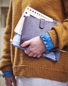 Person holding a planner and pen, wearing a mustard yellow sweater.