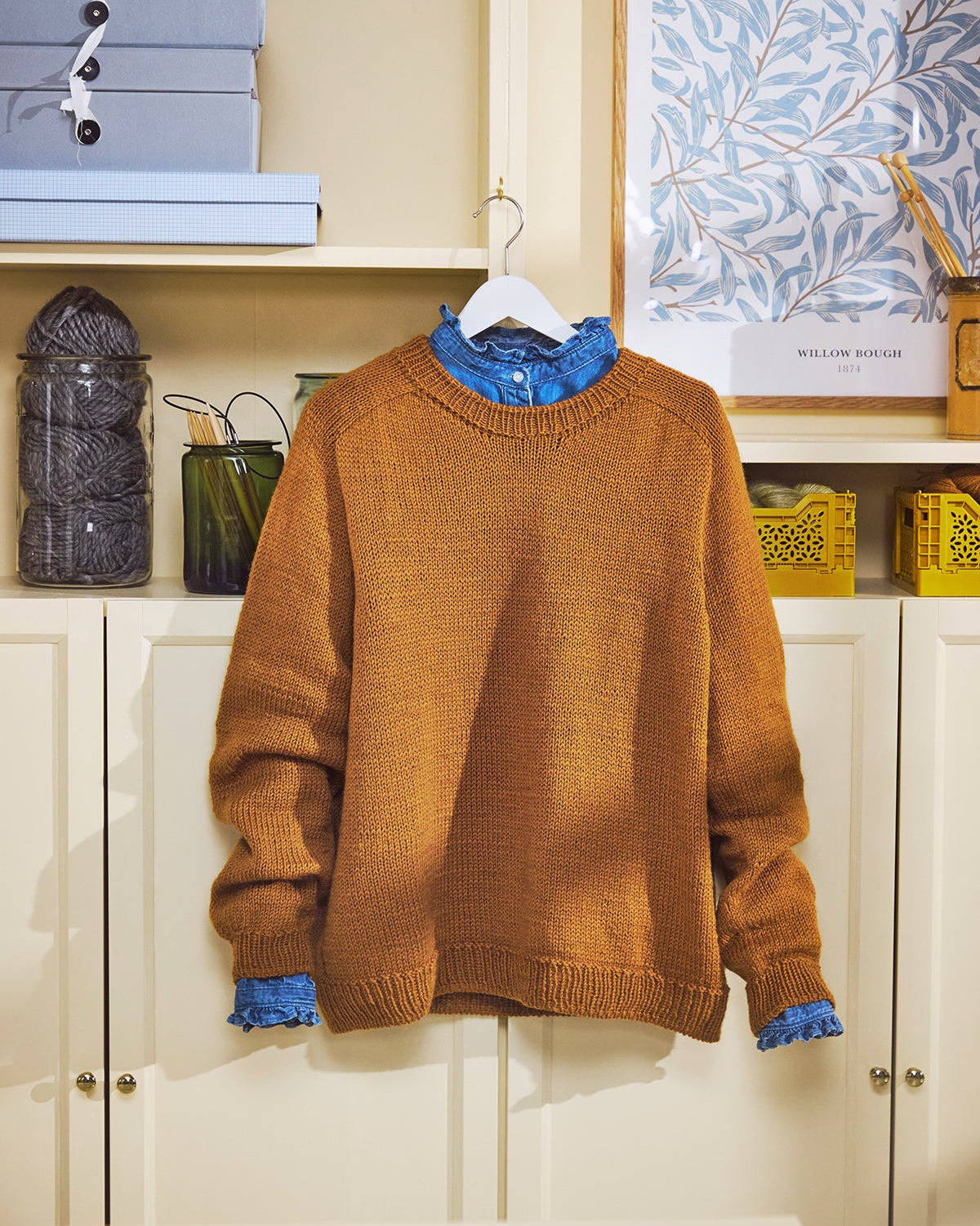 Brown sweater with blue trim hanging on a white hanger against a neutral background.